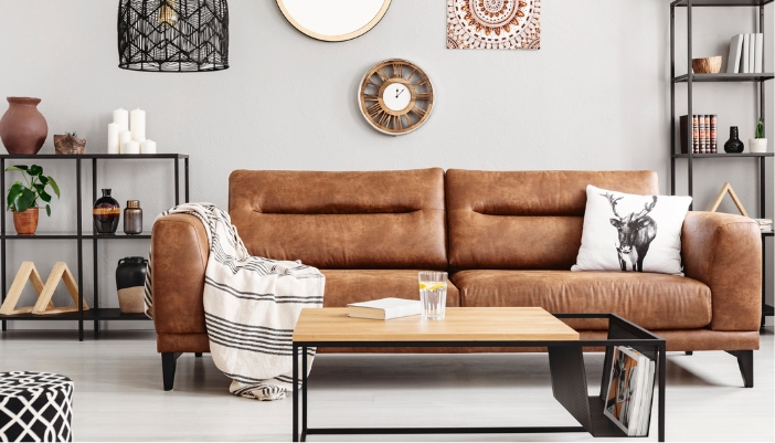 A brown leather couch sits in front of a wall of decor and has a white blanket and pillow on it.