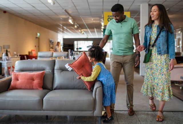 Front view of a family walking through a furniture store as their daughter jumps onto a sofa