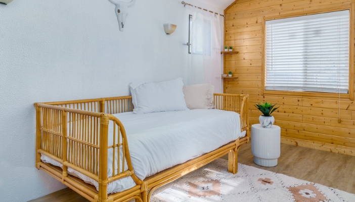 A wooden day bed in a cabin-type room with plants and white accents.