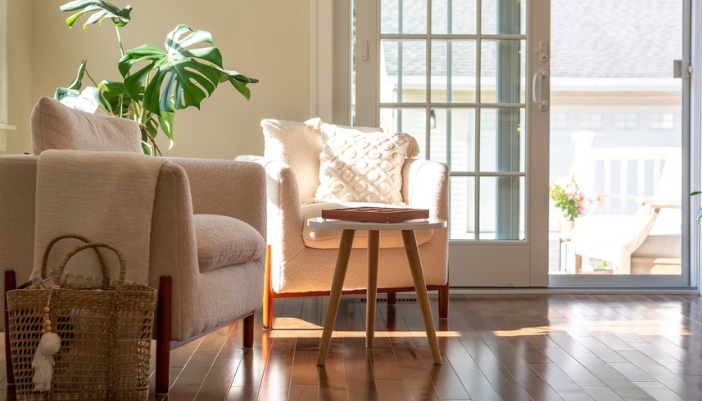 Two cream upholstered armchairs and a small wooden side table beside sunlit glass patio doors