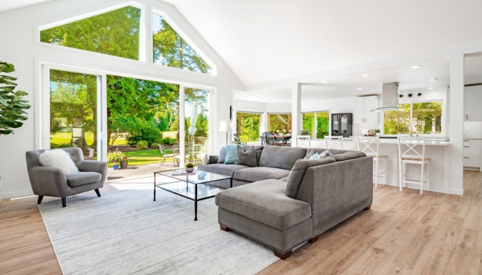 Open-concept living room with a gray sectional, gray accent chair, and glass-top coffee table beneath tall peaked windows