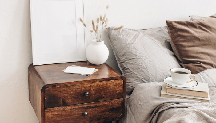 Dark wood two-drawer nightstand with a glossy finish beside a bed with gray linen bedding