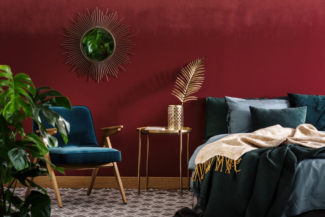 gold table between green armchair and bed in sophisticated red bedroom