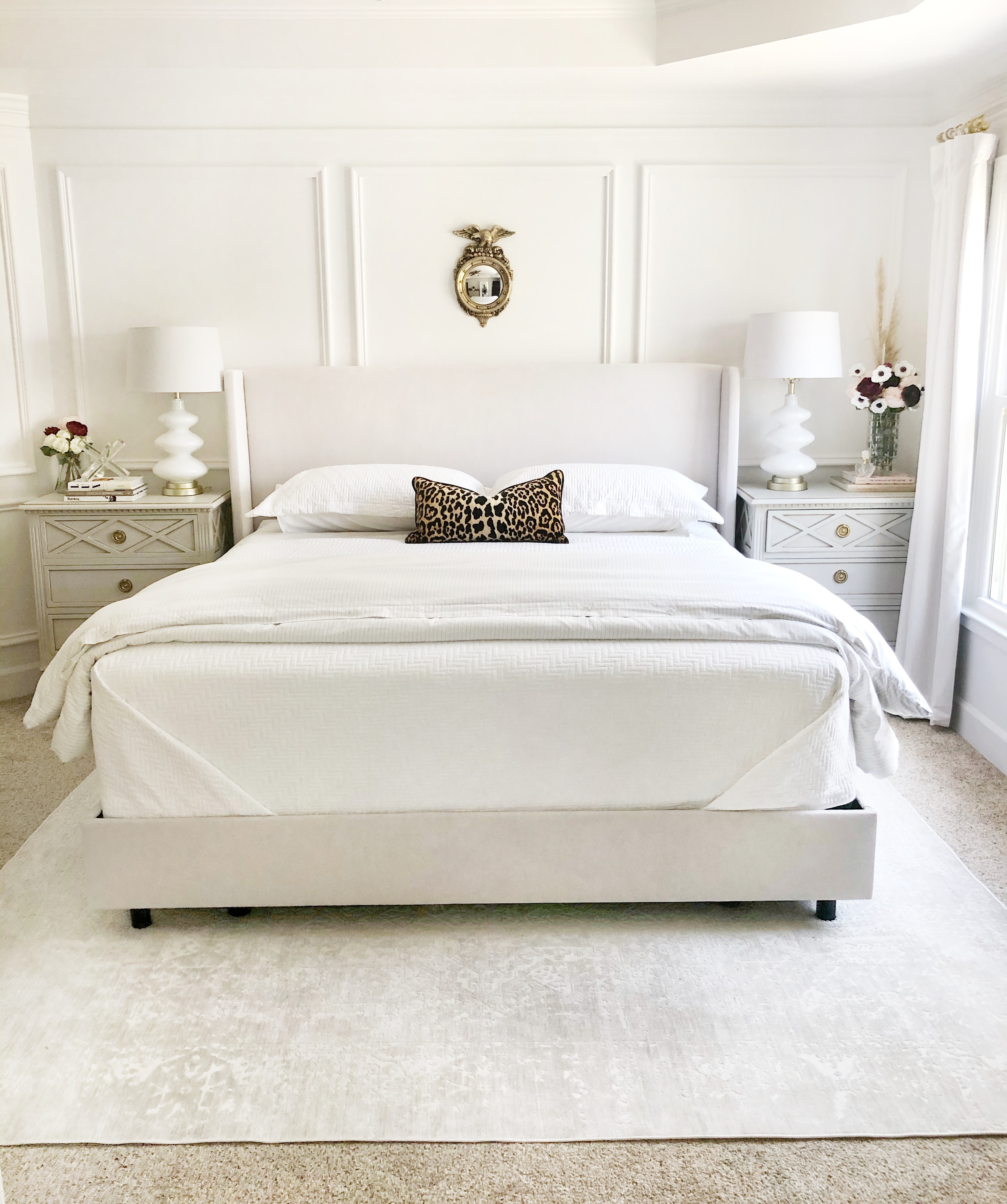 A tonal bedroom with a pair of matching nightstands, lamps, and flowers on either side of the bed