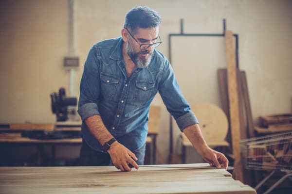 iStock Credit: svetikd A man in a denim shirt measuring a slab of wood