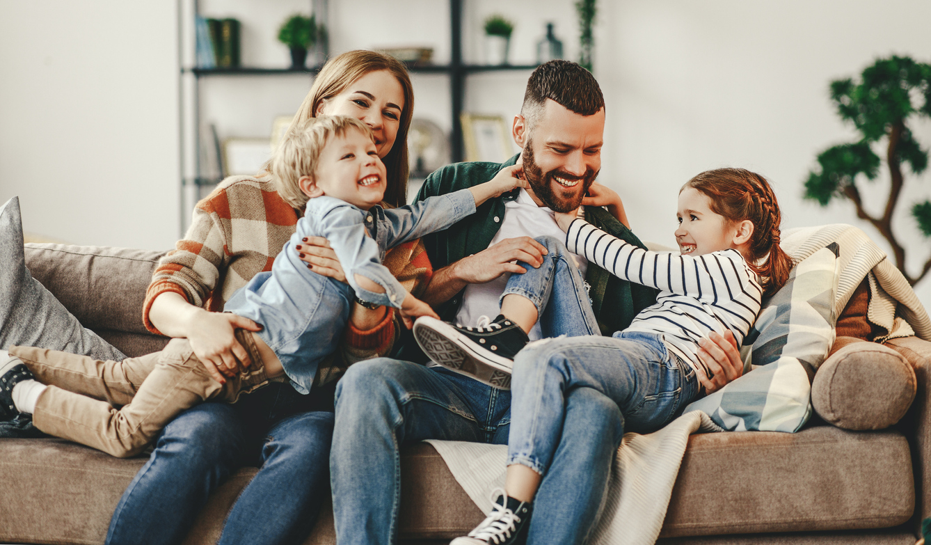 family of four seated together on a sofa laughing and playing 