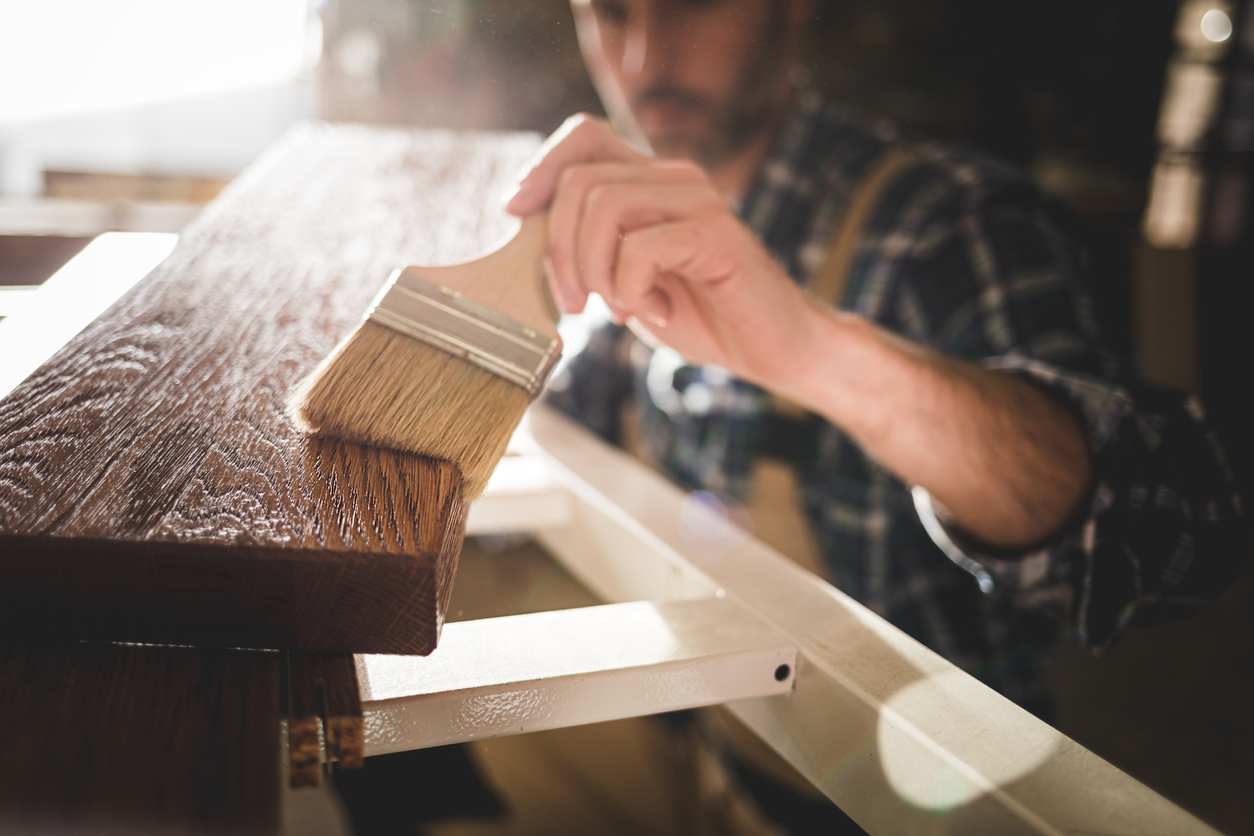 iStock Credit: leszekglasner paintbrush applies paint or varnish on wooden board in carpentry workshop