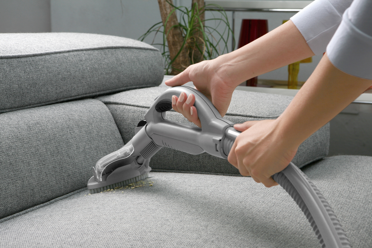 woman using stick vacuum on gray sofa