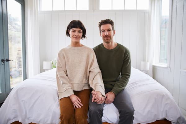 A woman and man on a bed holding hands looking into a camera A woman and man on a bed holding hands looking into a camera