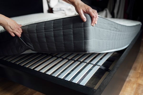 A person lifting a mattress, exposing bed slats