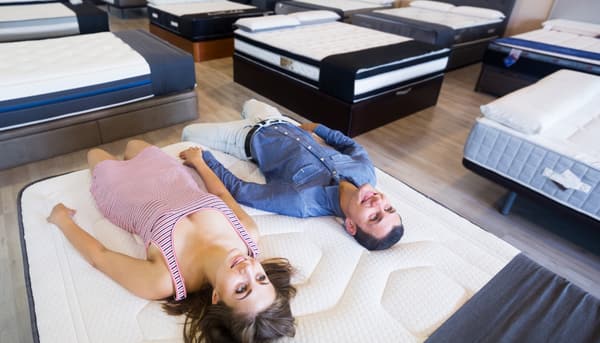 A woman and a man smiling while trying a mattress in a store A woman and a man smiling while trying a mattress in a store