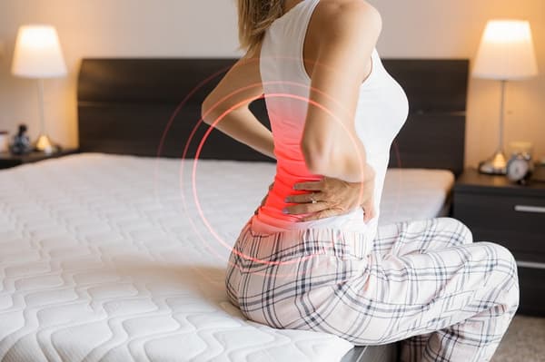 iStock Credit: grinvalds A woman grabbing her lower back while sitting up in a bed