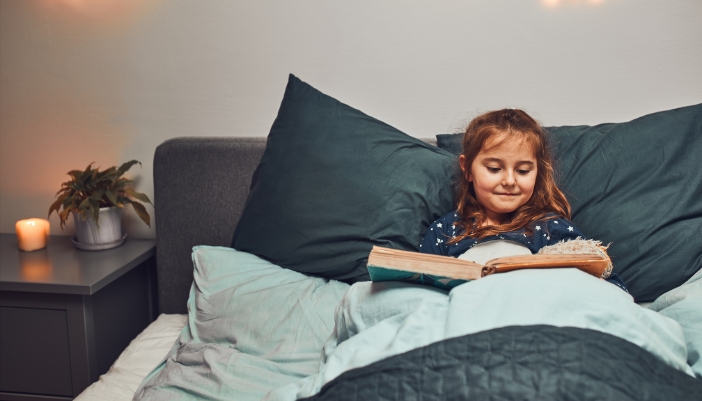 Matt_Reading-Before-Bed_1.jpg Little girl smiling as she reads a big book in bed