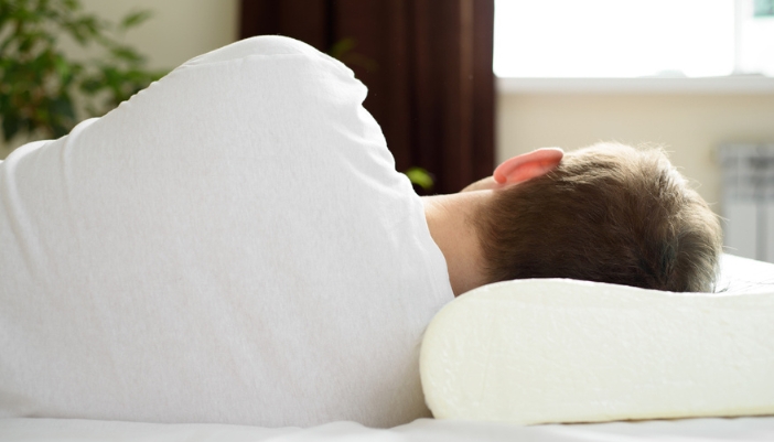 A man lays on his side and uses an ergonomic pillow.
