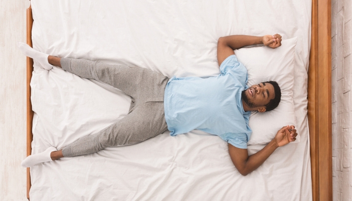 A man lays on his back on a bed with white sheets. 