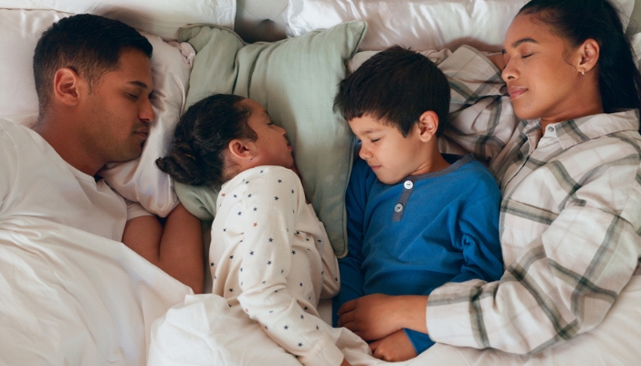 A man, woman, and two children sleep in a bed together.