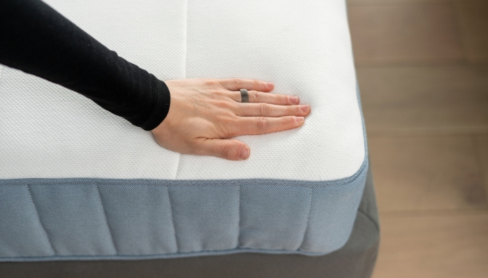 A hand presses down on a mattress to check firmness.