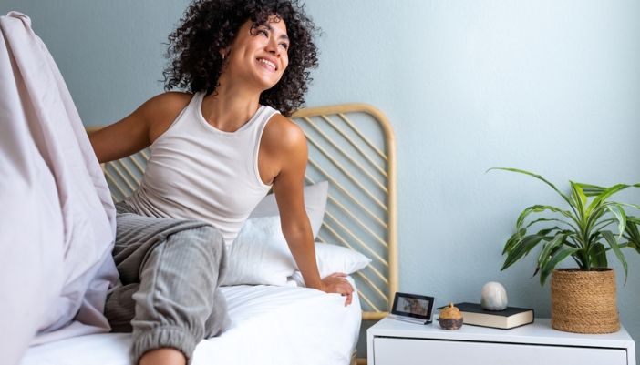 A well-rested woman happily gets out of bed in the morning.
