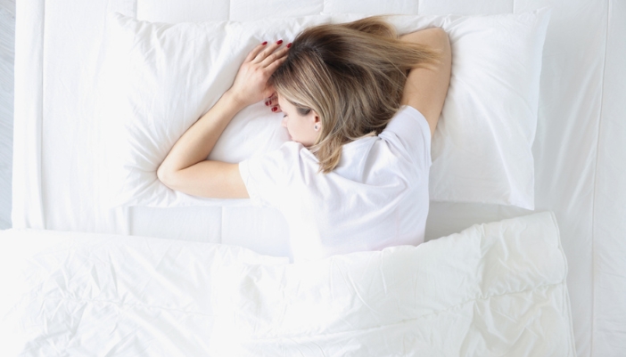 A blonde woman lays on her stomach to sleep.