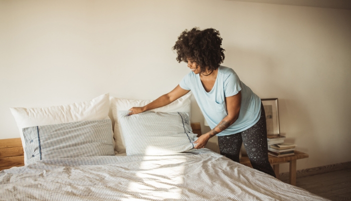 An older woman makes her bed in the morning and fluffs the pillows. 