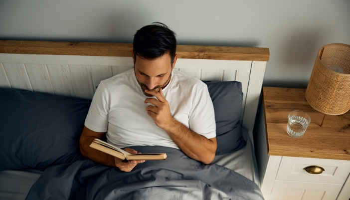 A man lays in bed and reads his book.