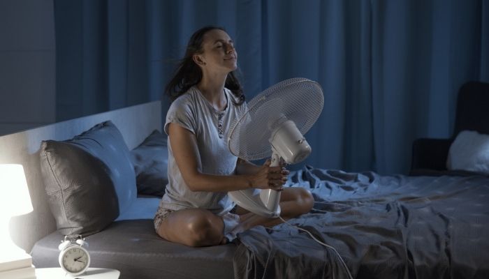 woman using fan while on bed