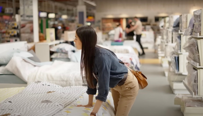 A young woman presses down on a mattress in a showroom.