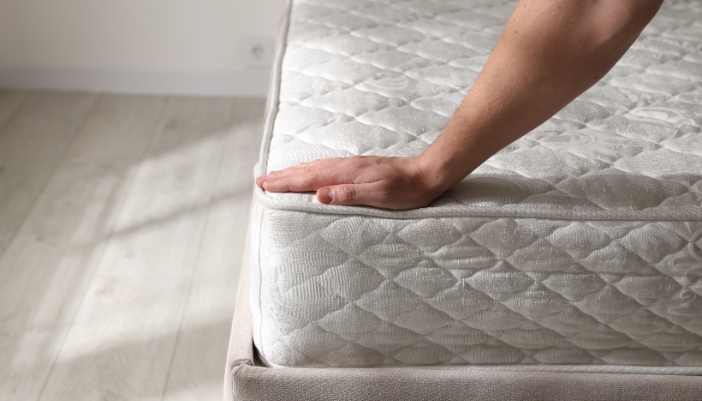 A hand is on a blank mattress in an empty room.