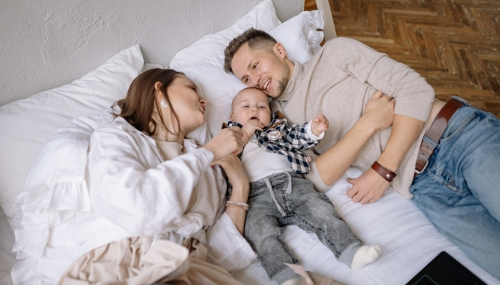 A man, woman, and child lay in their bed at home.