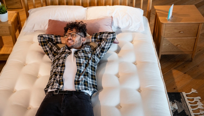 A young man lays back on a mattress in a showroom.