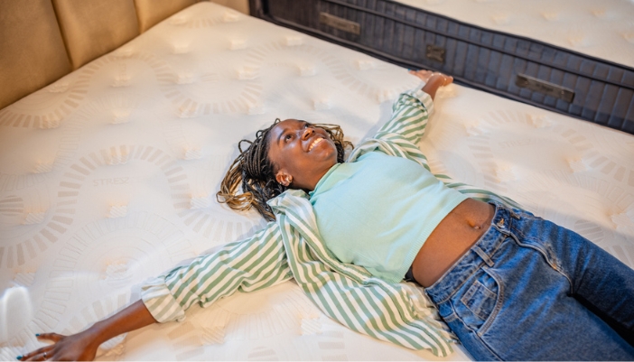 A young woman lays back on a mattress in a showroom.
