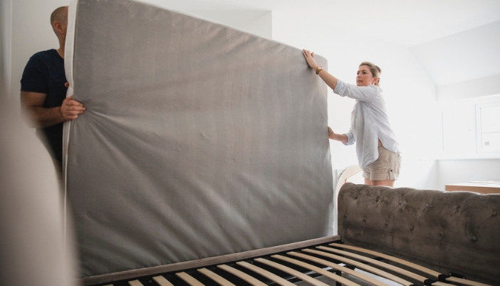 A couple rotates their mattress in their home bedroom.