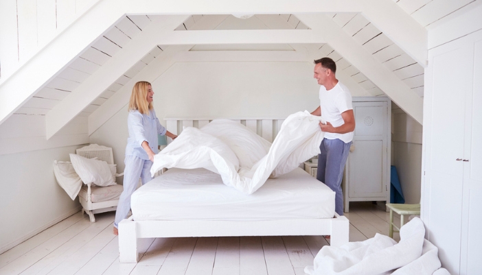 A middle-aged couple makes their bed together happily.