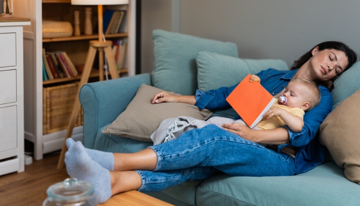 Mom and baby sleep sitting up on a couch after reading a book.