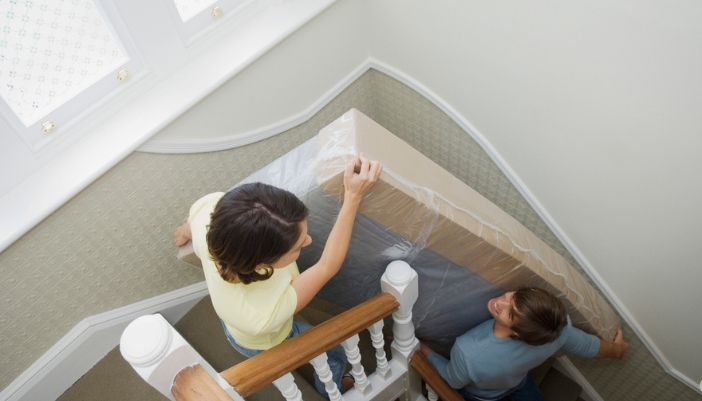 A couple moves a mattress up a tight staircase in their home.