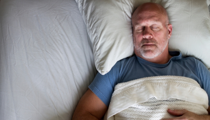 A man sleeps in a dark room on his back.