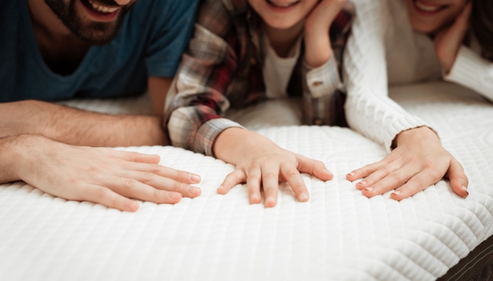A family lays on a mattress and presses down to test the firmness.