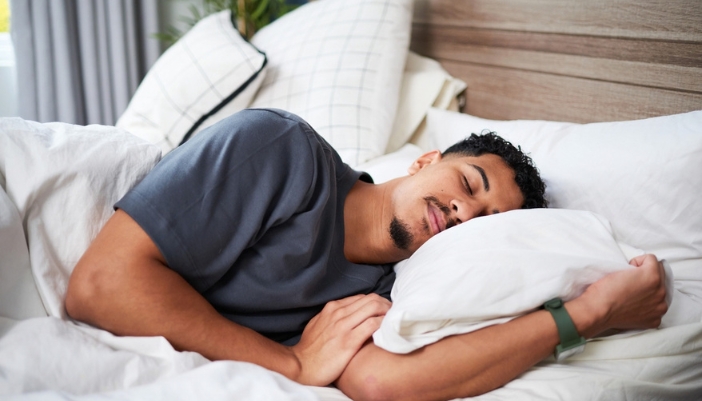 Man sleeping soundly on his side while hugging a white pillow in a bed with crisp white bedding