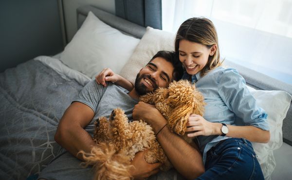 A smiling man and woman with a dog on a mattress 