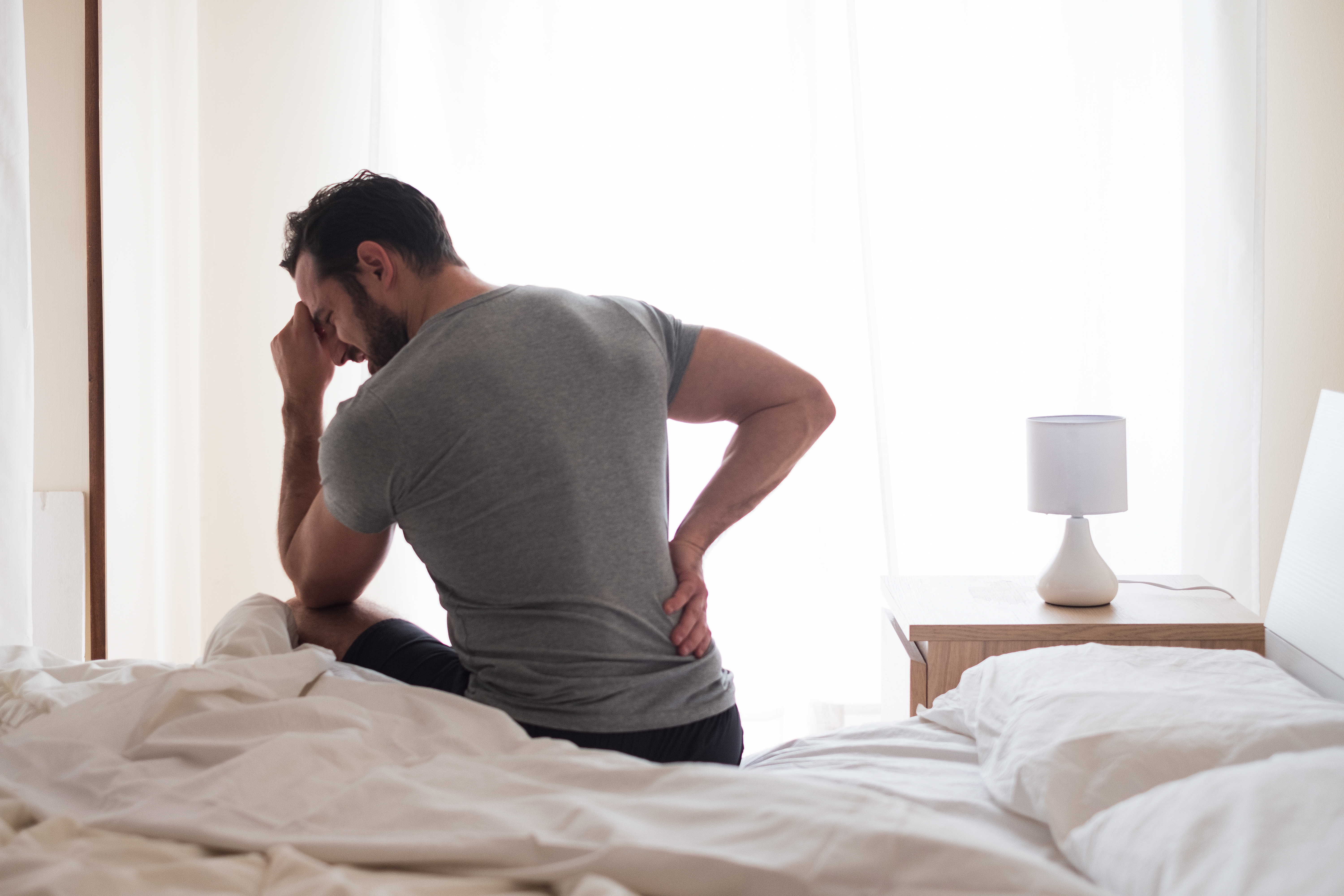 A man sitting up in bed grabbing his lower back in pain 