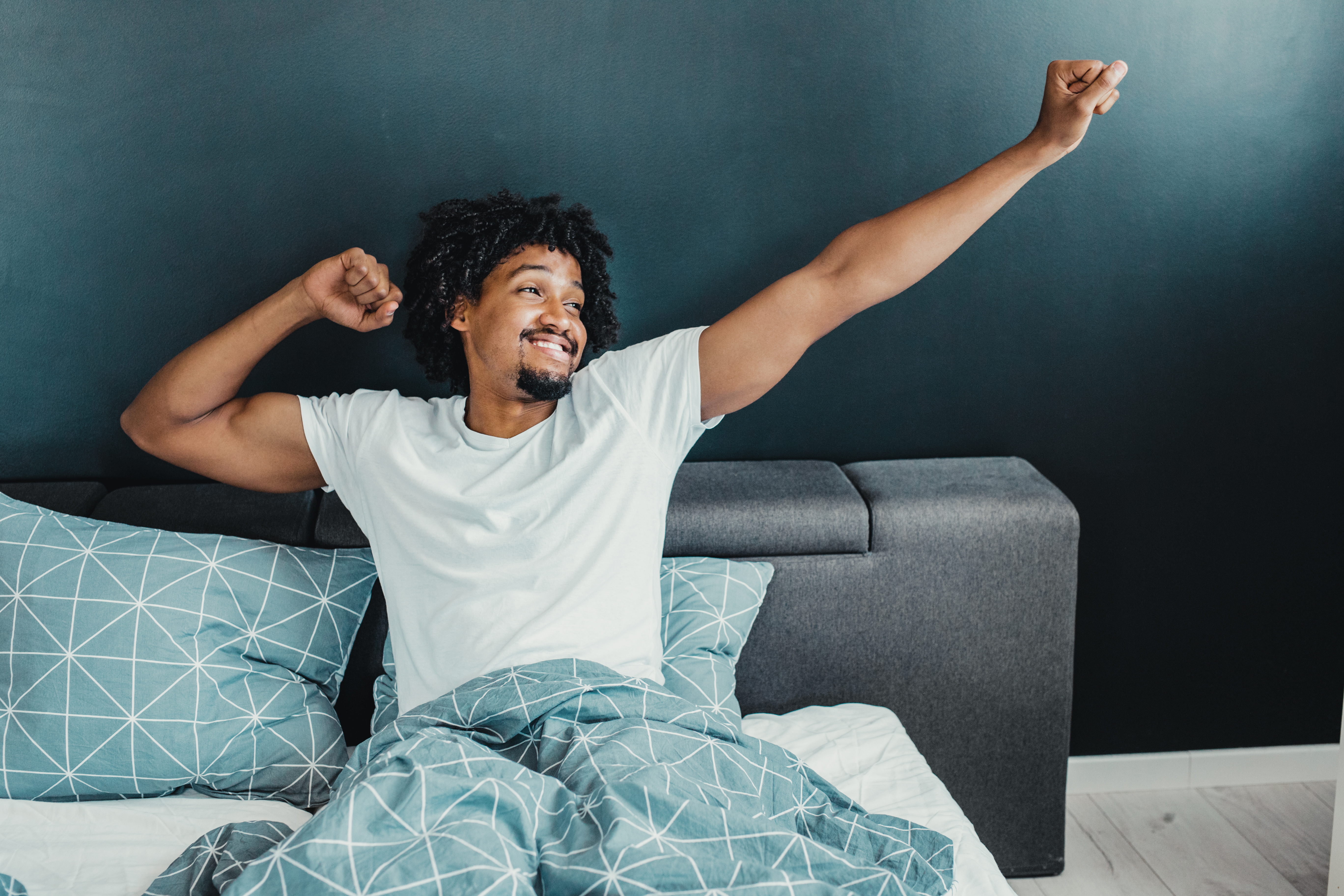 blackCAT Young man stretching and smiling in bed