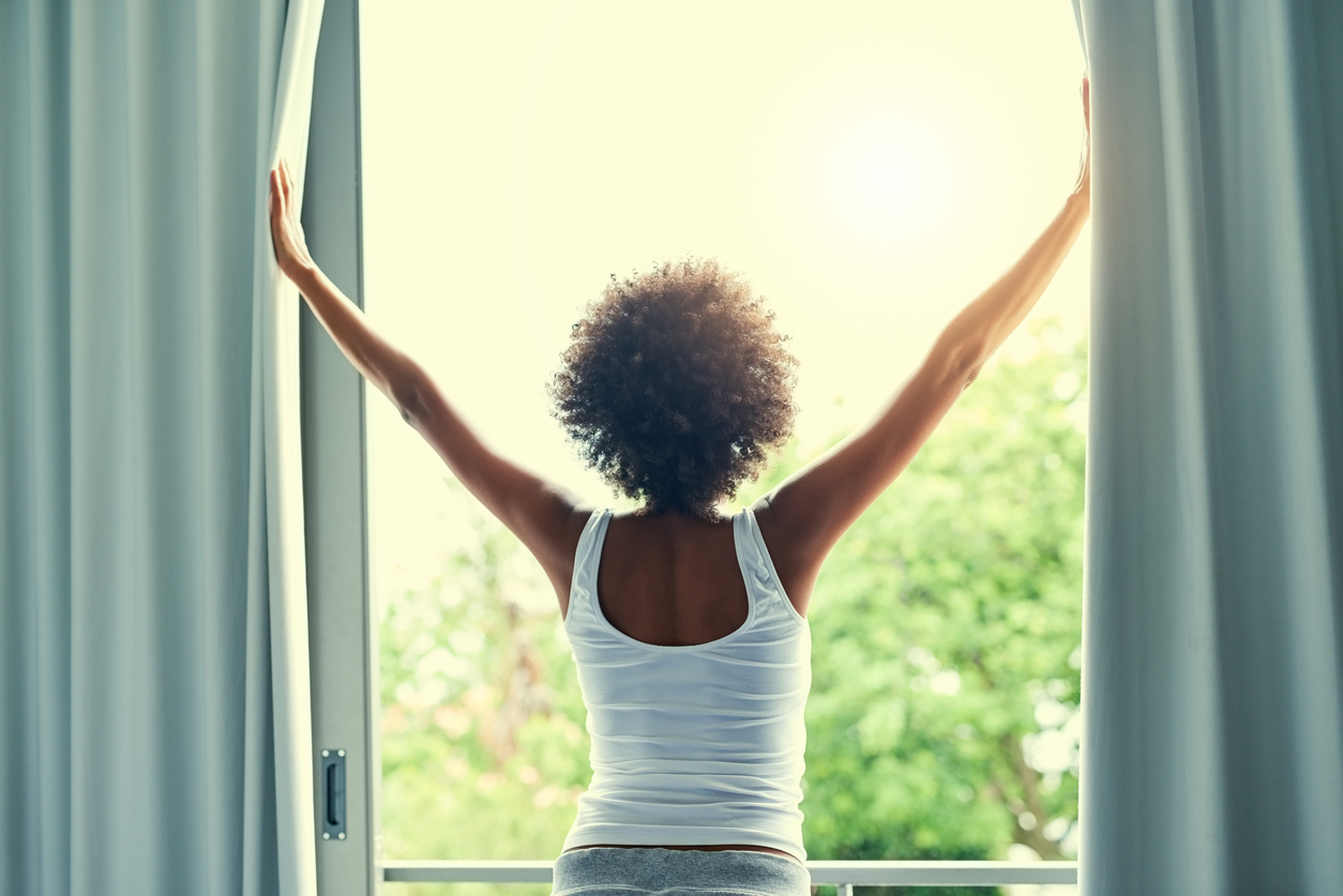 iStock Credit: PeopleImages woman throws open curtains to sunlight to greet the day