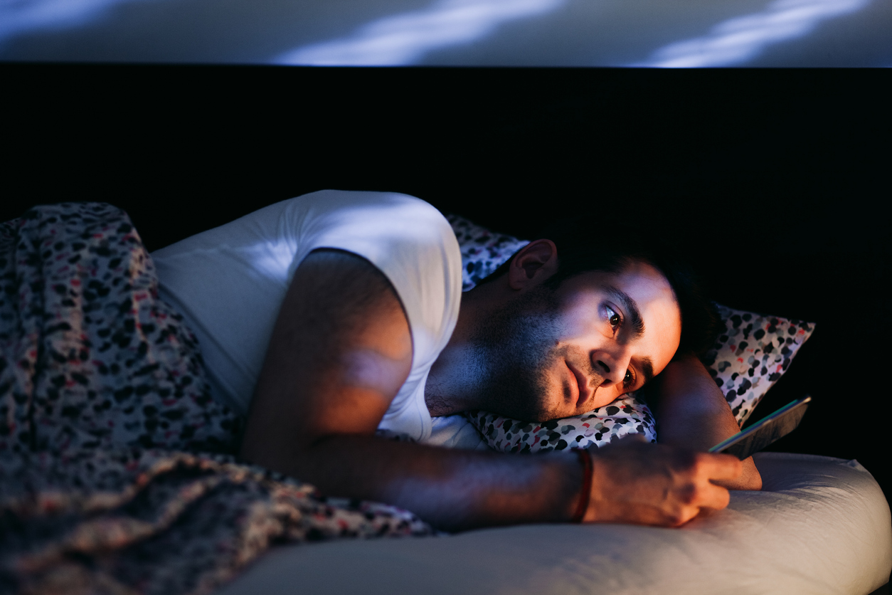 iStock credit: Marjan_Apostolovic Young man uses his phone in bed in a dark bedroom