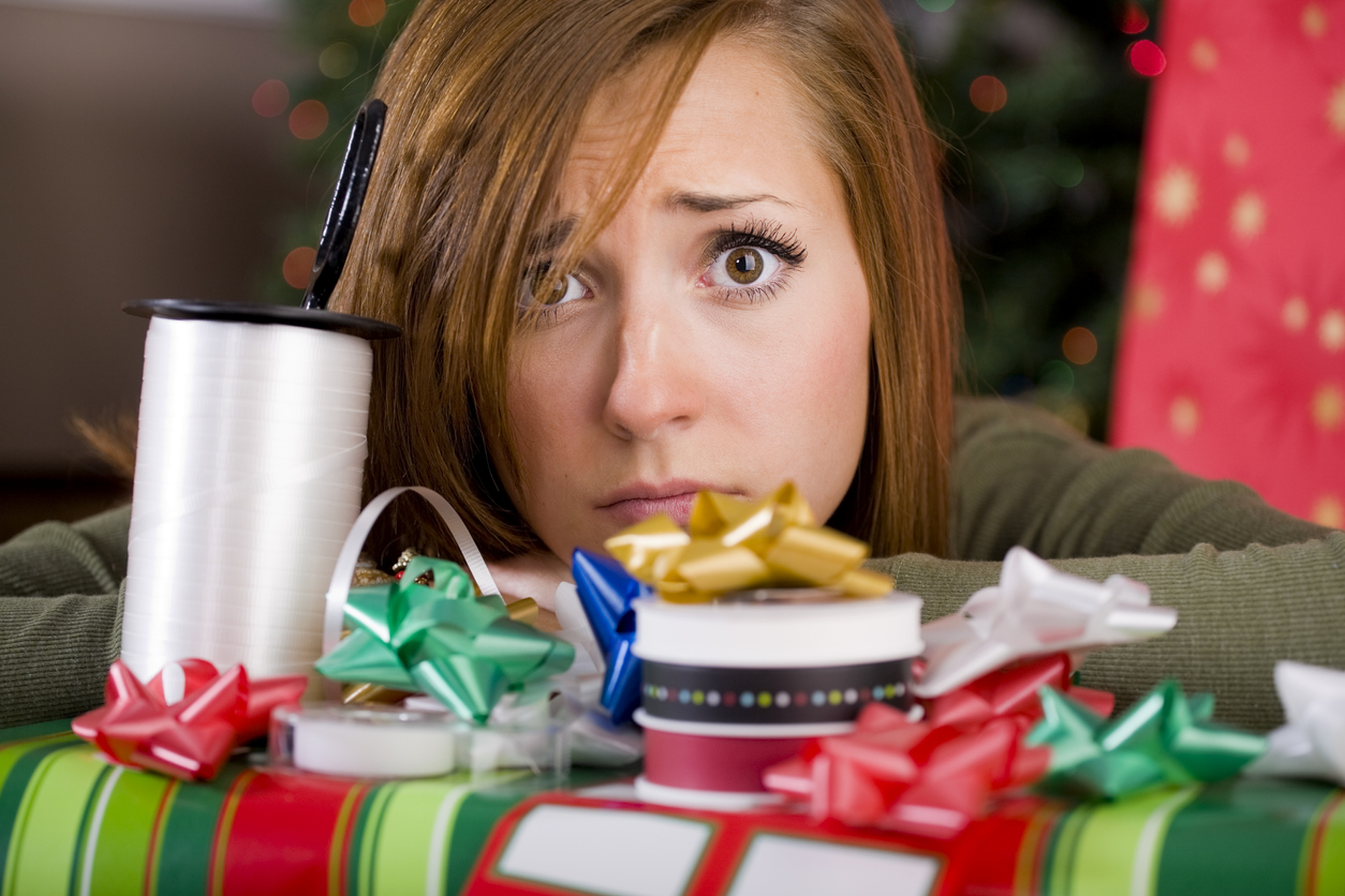 iStock Credit: RichLegg young woman wrapping Christmas presents in front of a Christmas tree