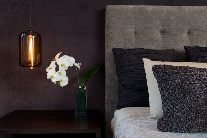 : a vase with white flowers on a nightstand next to bed and hanging pendant light 