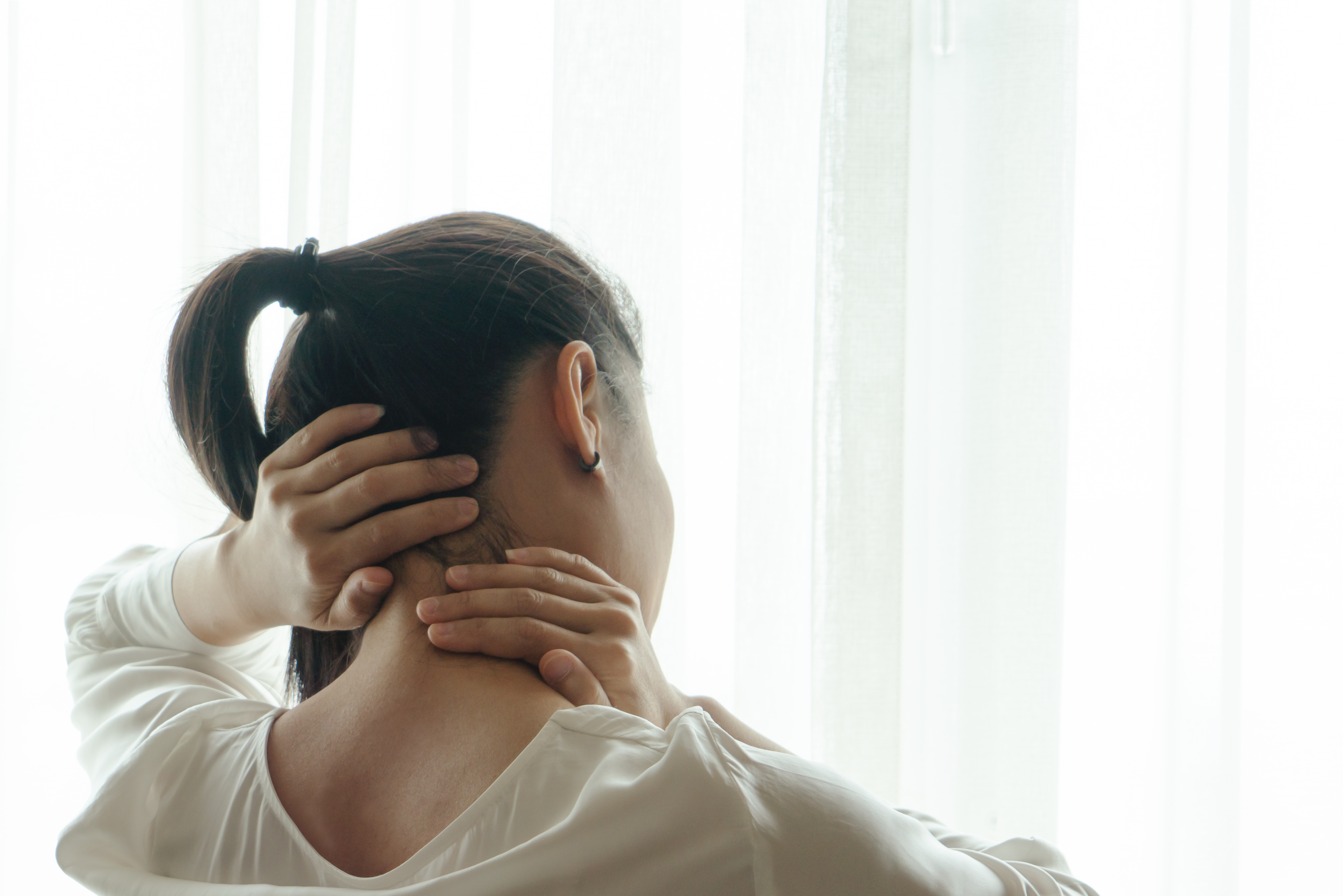 iStock Credit: PORNCHAI SODA Woman with ponytail grabs the back of her neck and massages it