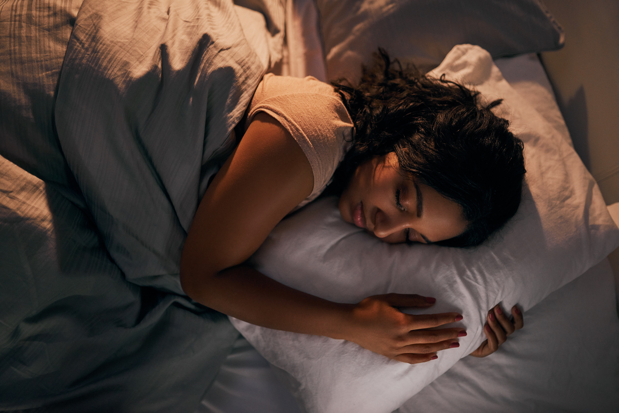 Woman sleeping in bed on her side with her a arms wrapped around a pillow