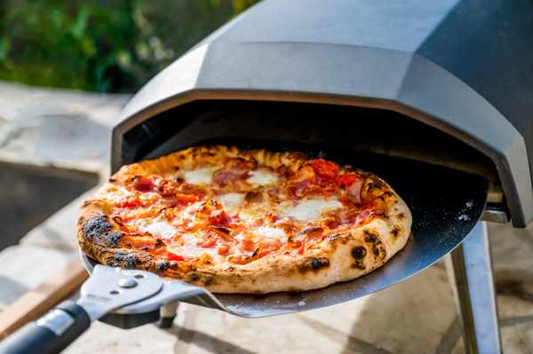A close-up of a pizza being pulled out of an outdoor pizza oven
