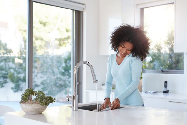 Credit: iStock Front view of a Woman on the phone washing a dish in her sink with a pull down faucet