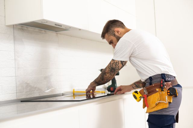 Front view of a handyman installing a flat-top cooktop in a kitchen